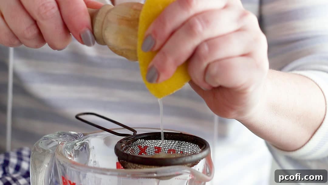 Fresh lemons being juiced through a fine-mesh sieve into a measuring cup, ensuring a smooth, pulp-free lemon meringue pie filling.
