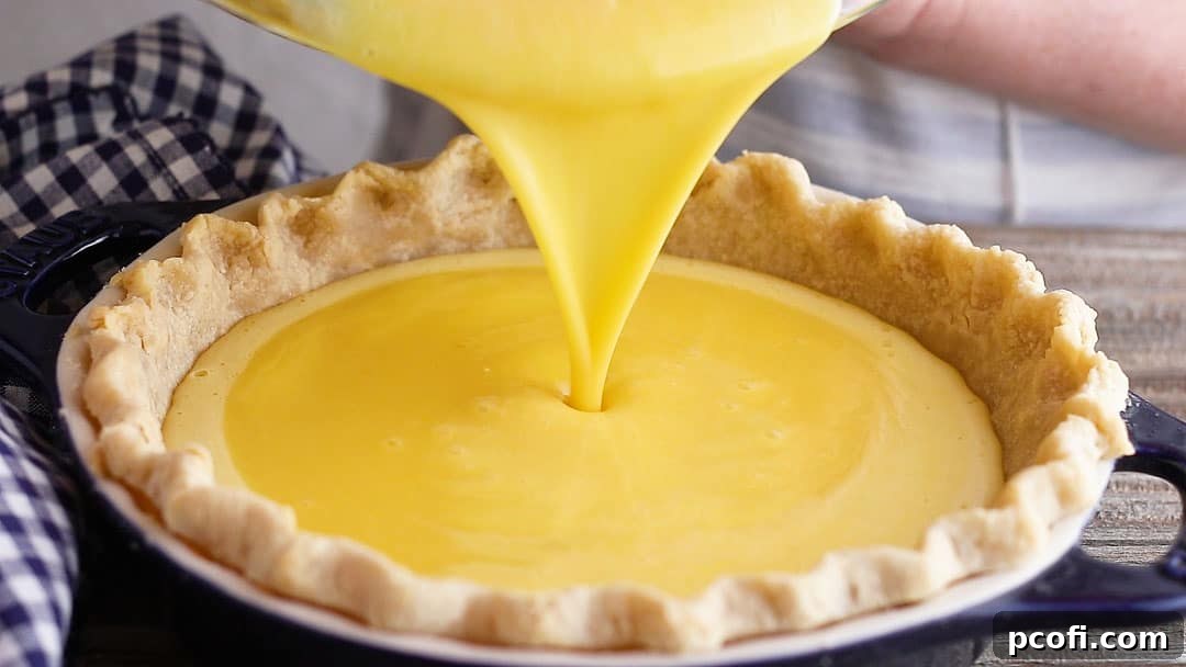 Pouring the bright yellow lemon pie filling into a golden, pre-baked pie crust, ready for its transformation in the oven.
