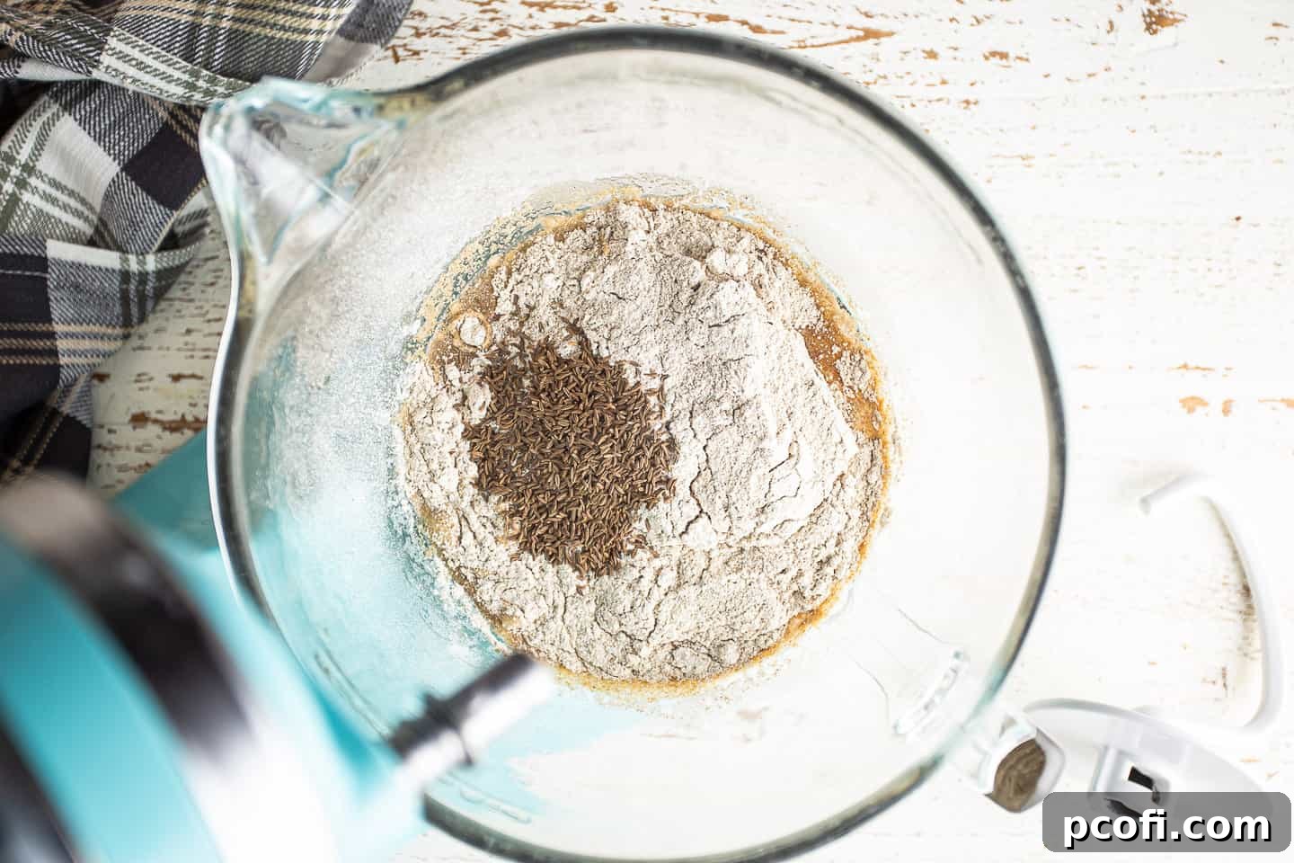 Adding rye flour, caraway seeds, and salt to the liquid ingredients.