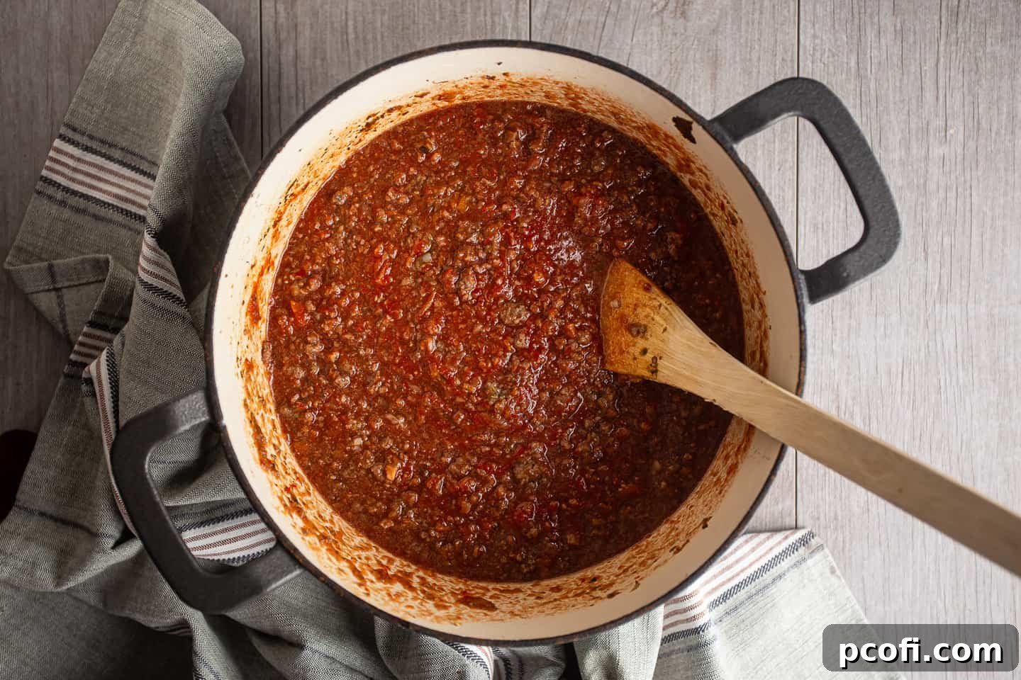 Bolognese sauce gently simmering over low heat with the pot lid partially ajar, allowing steam to escape.