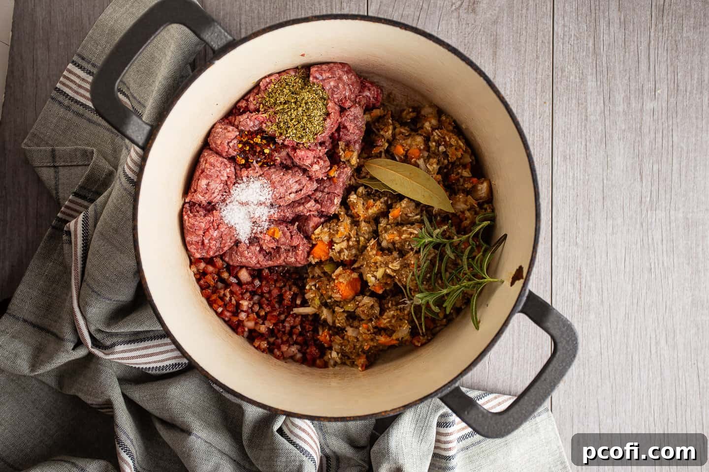 Ground meat, processed vegetables, herbs, and seasonings being added to the pot for Bolognese sauce.