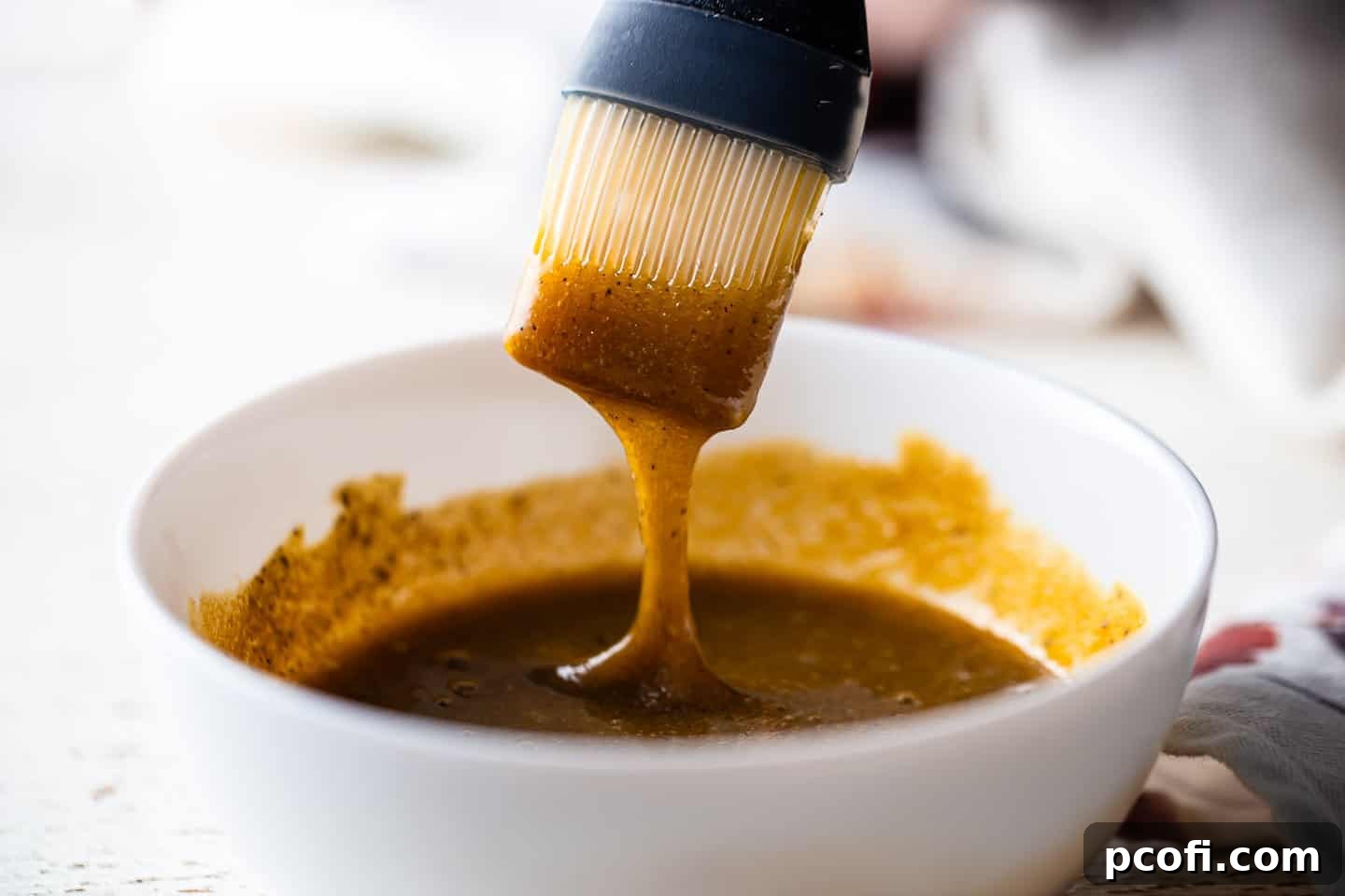 A silicone basting brush is dipped into the rich brown sugar and Dijon ham glaze, picking up a generous amount for application.