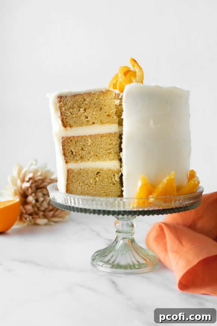 A slice of orange creamsicle cake on a small white plate, with the rest of the cake in the background.