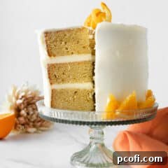 three layer orange creamsicle cake with slice cut on cake stand with orange napkin.