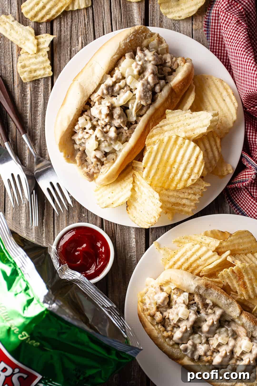 Chicken cheese steaks served with chips on a distressed wooden tabletop.