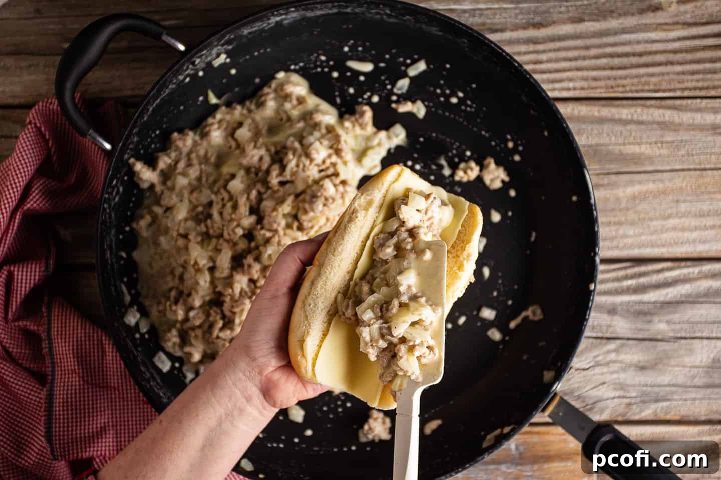 Scooping chicken cheesesteak sandwich filling into rolls.