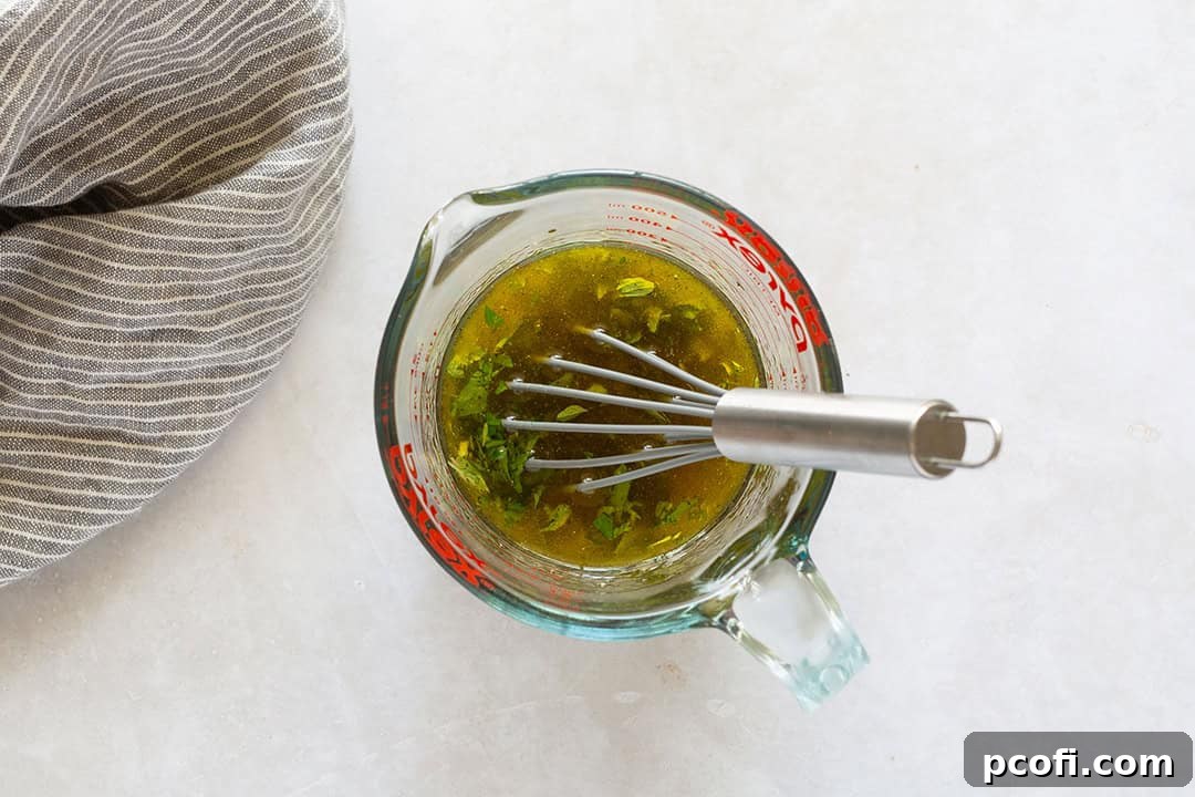 Greek salad dressing in a liquid measuring cup with a whisk, showing the emulsified vinaigrette.