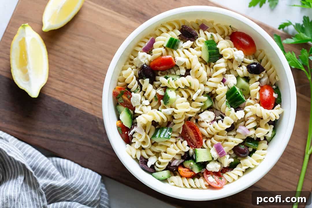 A landscape photo of a large bowl of Greek chicken pasta salad, garnished with lemon slices and fresh parsley, ready for serving.