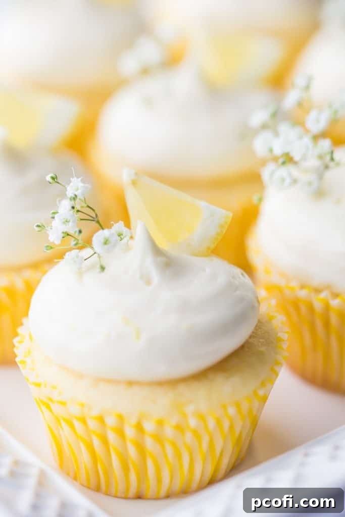 Vertical image of lemon cupcakes with lemon curd filling and lemon cream cheese frosting, garnished with lemon wedges and baby's breath.