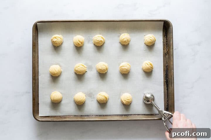 Lemon cookie batter being scooped onto a sheet pan