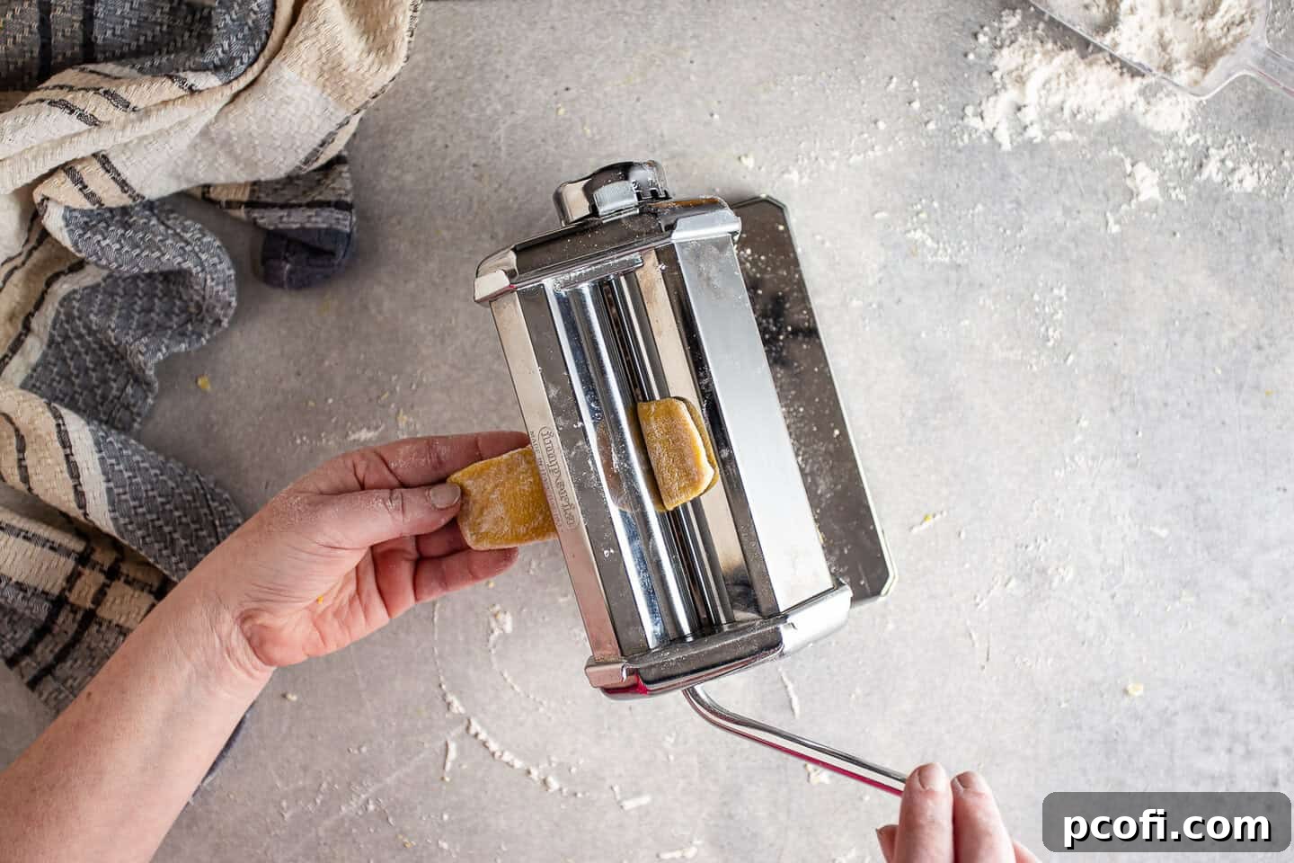 Running homemade pasta dough through the roller machine on the thickest setting to begin flattening.