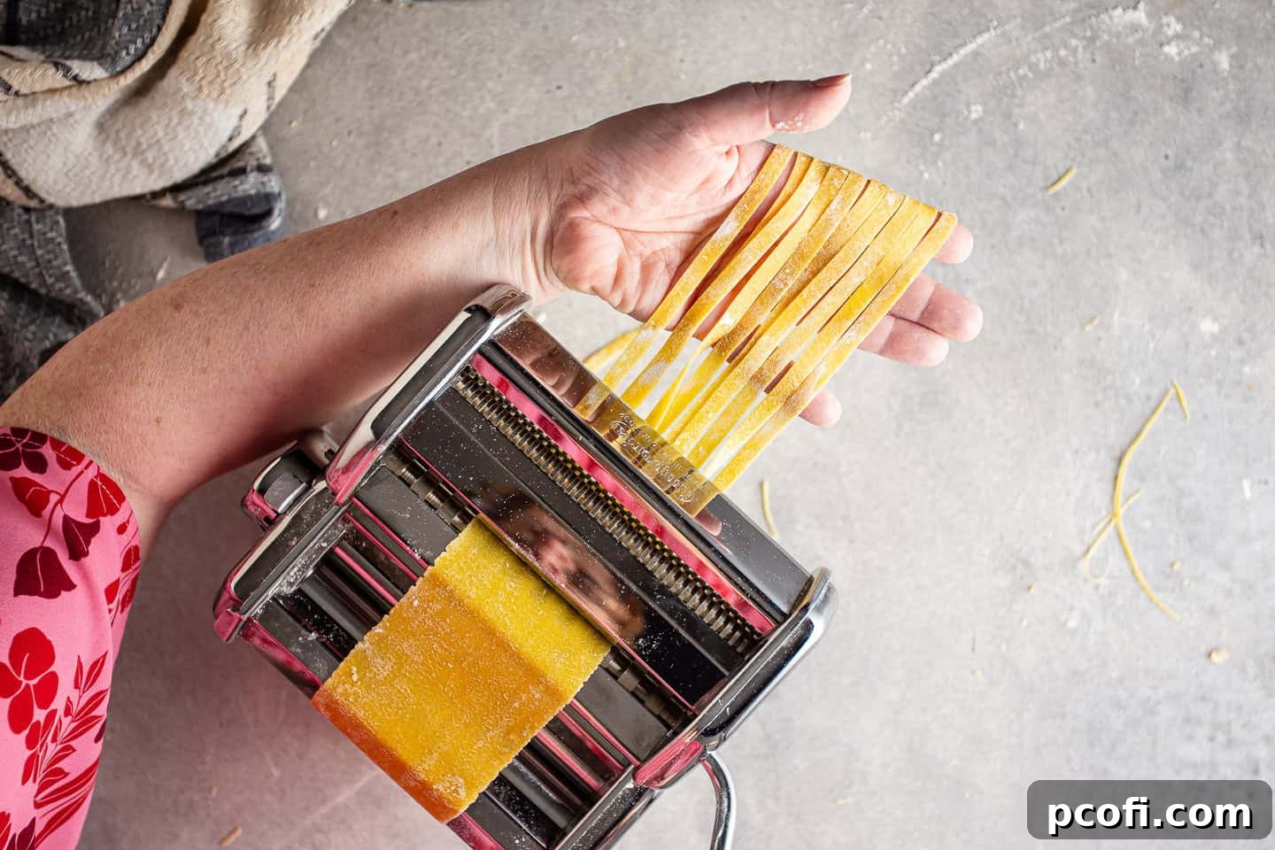 Cutting homemade pasta sheets into wide noodles with a pasta maker attachment.