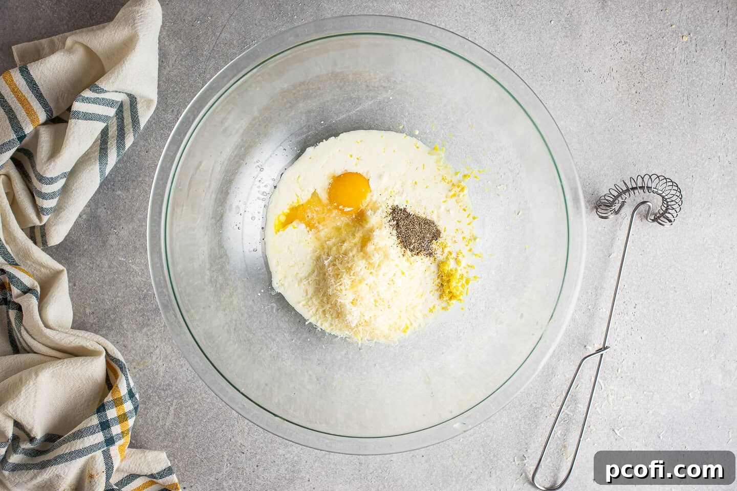 All the creamy lemon pasta sauce ingredients – including bright egg yolks, rich cream, savory Parmesan, fragrant lemon zest, tangy lemon juice, salt, and pepper – are carefully placed in a large clear glass bowl, glistening and ready for whisking.