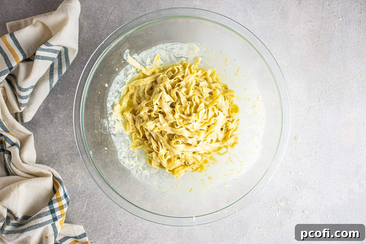 Freshly cooked pasta perfectly tossed in a creamy lemon sauce, presented in a large bowl, ready to be served. The sauce evenly coats each strand of pasta, creating a mouth-watering appearance. A fork is poised to serve.