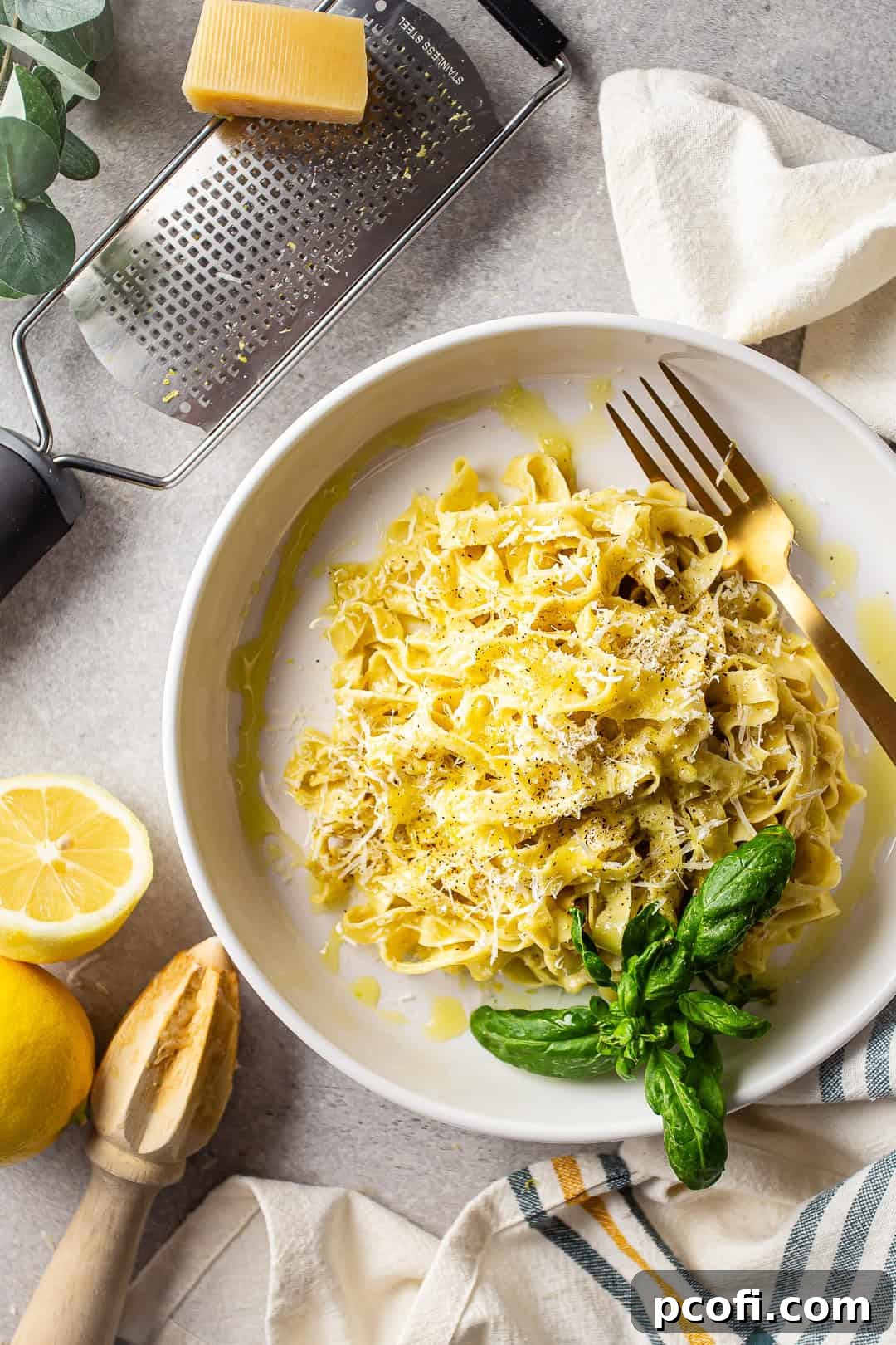 Creamy lemon pasta elegantly presented on a rustic gray tabletop, accompanied by fresh whole lemons and a block of Parmesan cheese, highlighting the main ingredients. The lighting is soft and inviting.