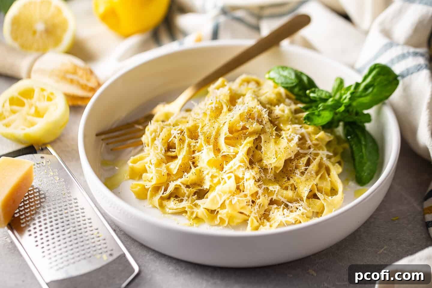 Lemon pasta, beautifully tossed with fresh homemade tagliatelle, presented in a bowl alongside a small dish of grated Parmesan, a bottle of olive oil, and a pepper mill, ready for garnishing. The dish looks fresh and vibrant.