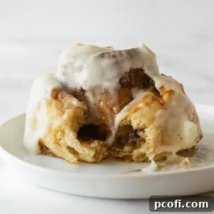 A crescent roll cinnamon roll with a bite taken, showing the cinnamon swirl and icing on a white plate.
