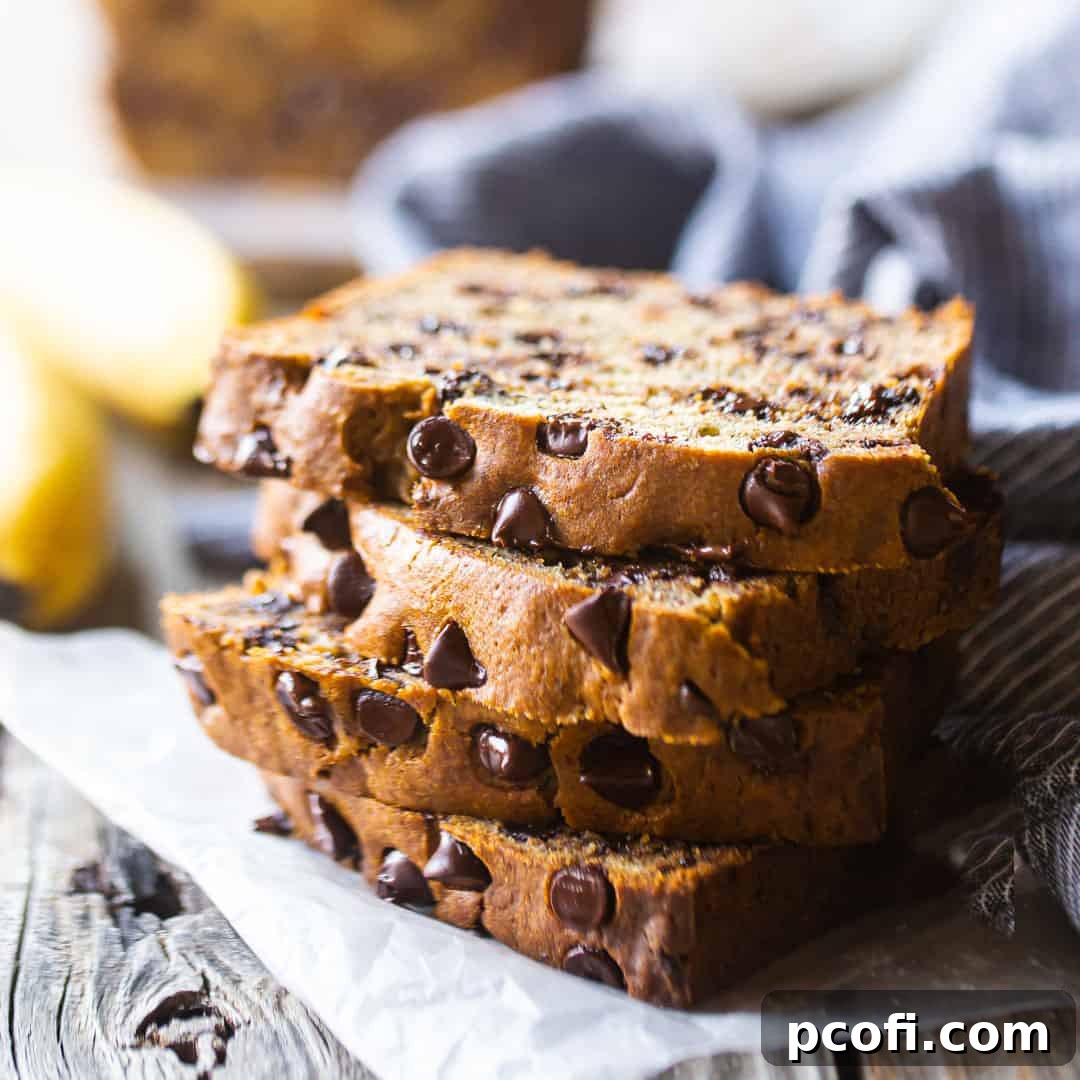 Chocolate chip banana bread slices stacked on a wood table with fresh bananas in the background.