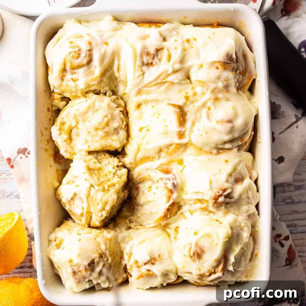 Orange sweet rolls in a white baking dish topped with cream cheese icing.