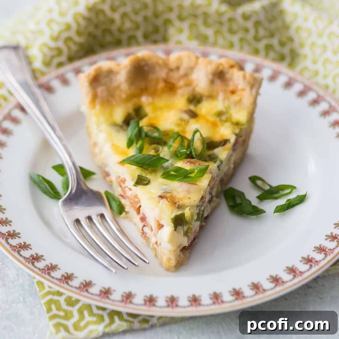 A slice of Quiche Lorraine on a china plate with a green printed napkin, showing the flaky crust and filling.