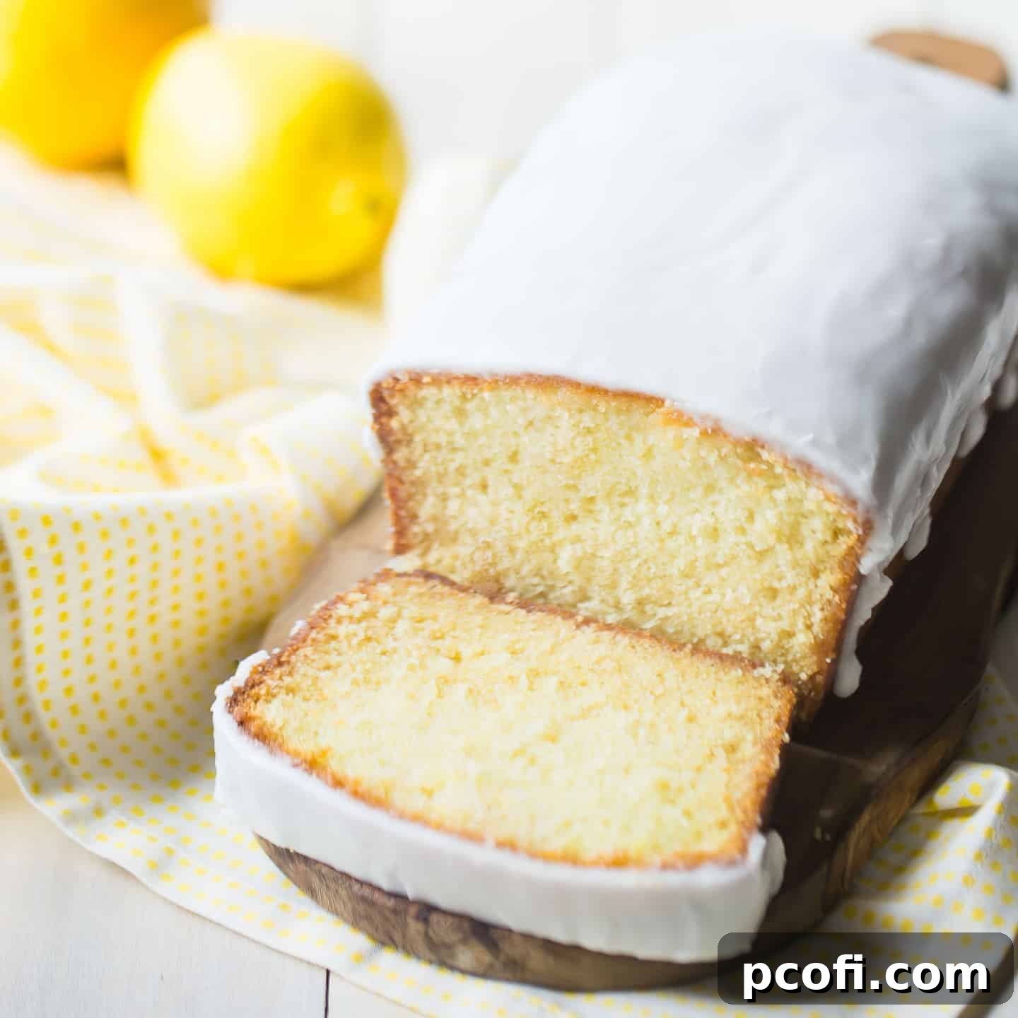 Iced lemon loaf on a wood cutting board with fresh lemons in the background, ready to be served.