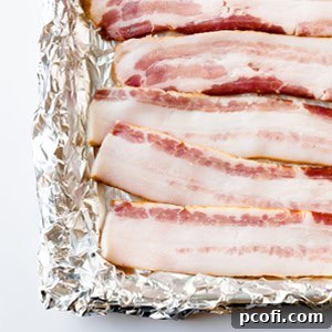 Crispy bacon slices arranged neatly on a foil-lined baking sheet, freshly cooked from the oven.