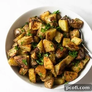 Golden brown oven roasted potatoes in a white serving bowl with a spoon.