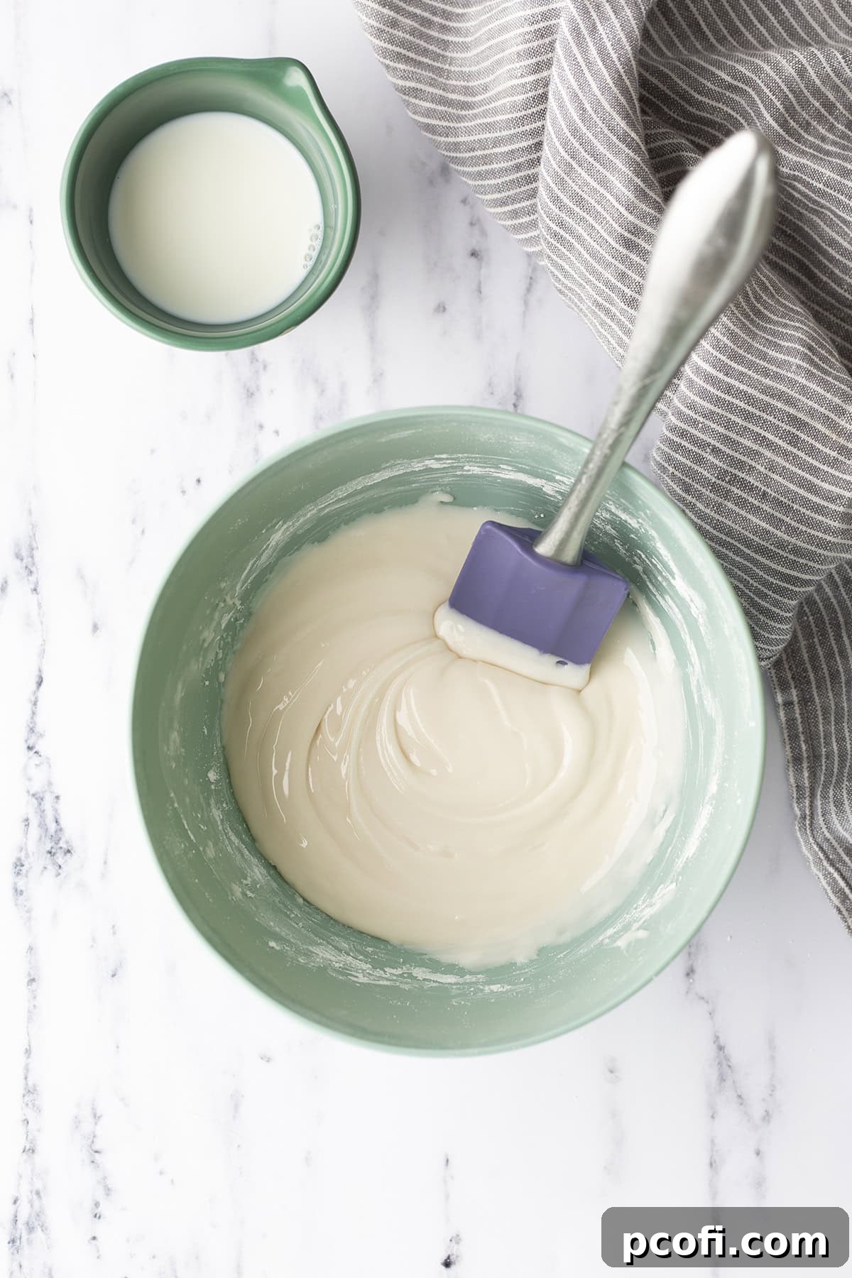 A bowl of vanilla glaze being stirred with a spatula, showing its smooth consistency.