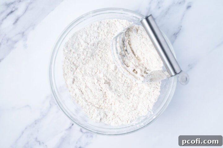 Grated butter thoroughly cut into flour in a mixing bowl with a pastry cutter, creating a coarse meal texture.