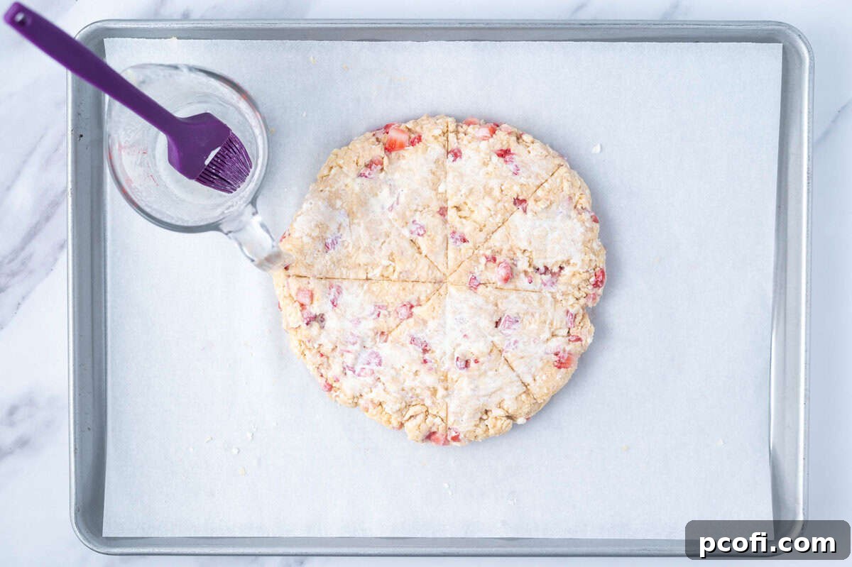 Strawberry scones expertly arranged in a circle and cut into eight triangles on a parchment-lined baking pan, ready for the oven.