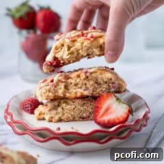 A hand reaching for a freshly baked strawberry scone from a plate, beautifully glazed and ready to enjoy.