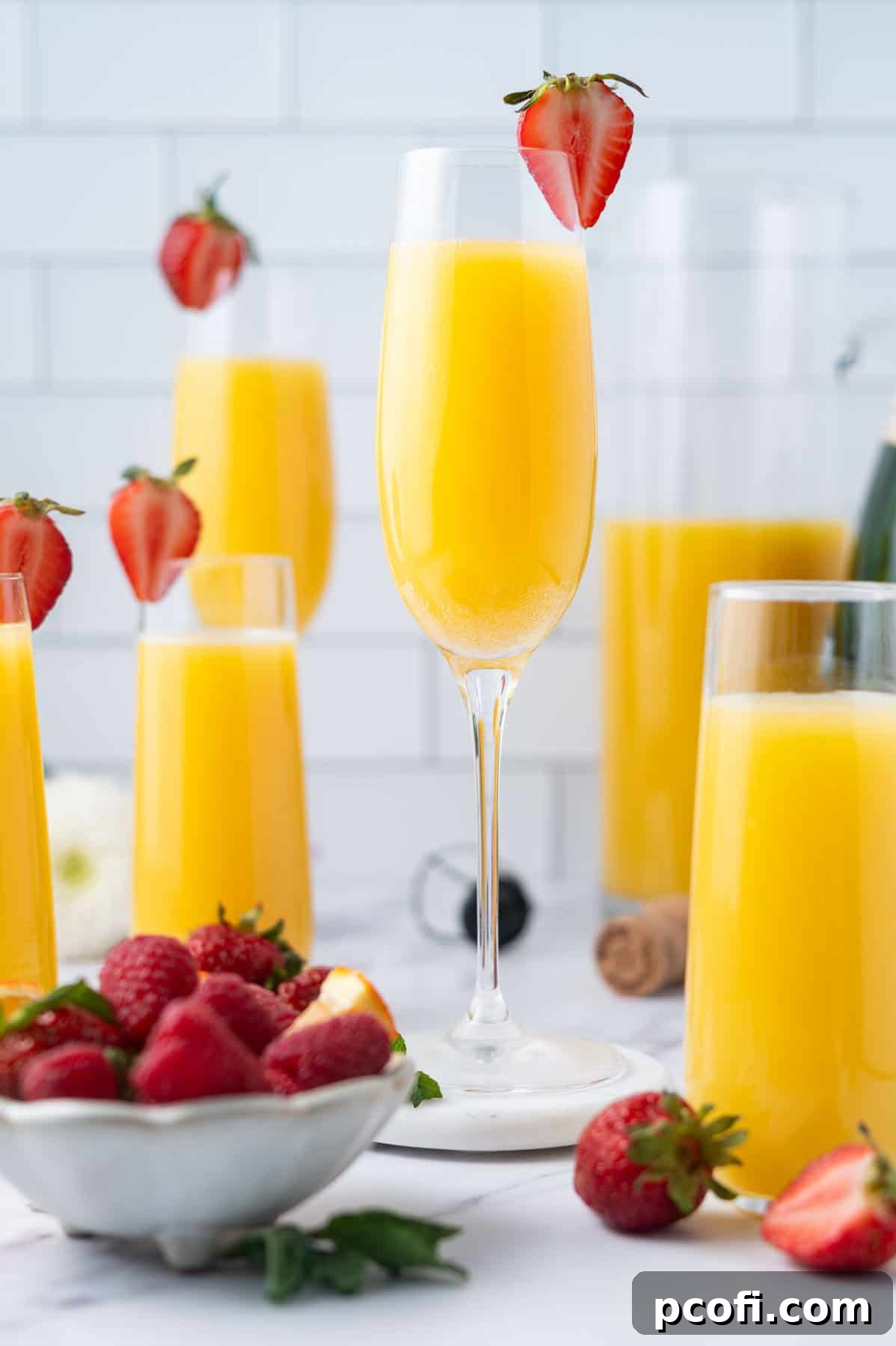 Champagne flute with a mimosa and a strawberry garnish, surrounded by other mimosas and brunch decor.