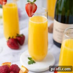 Mimosa cocktail with a fresh strawberry garnish on a coaster.