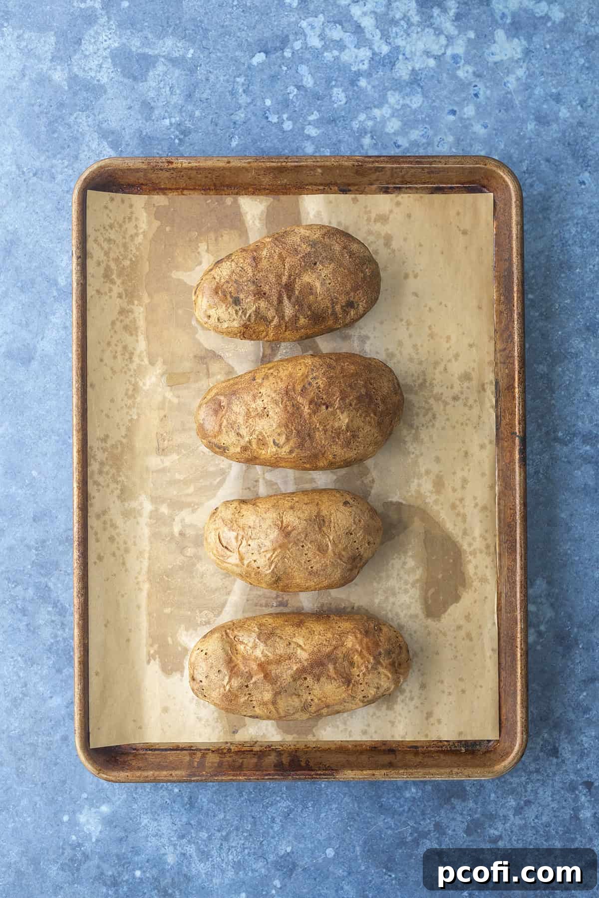 Baked potatoes with crisp skins cooling on a baking pan