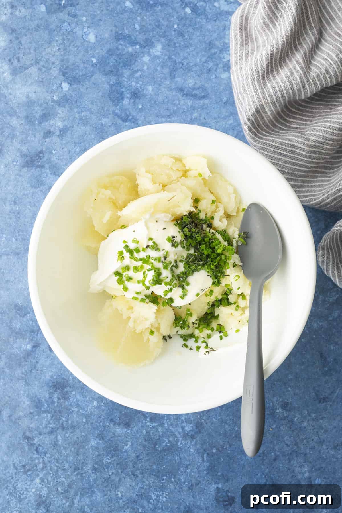 Potato flesh mashed in a bowl with sour cream, butter, herbs, salt, and pepper