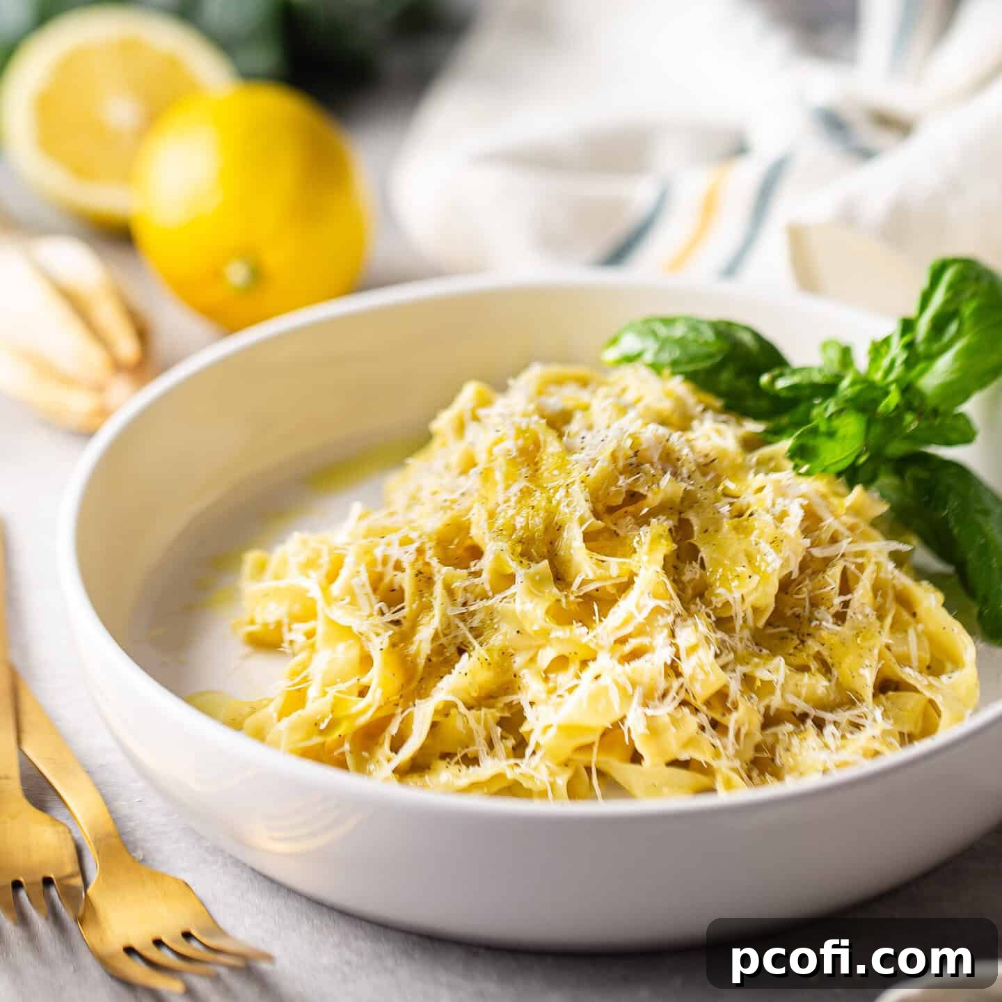 A tangle of bright lemon pasta in a shallow bowl with a sprig of fresh basil, indicating a refreshing and zesty dish.