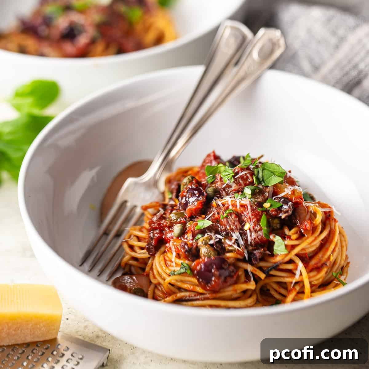 Spaghetti alla puttanesca nestled into a white ceramic bowl, showcasing its rich, robust sauce with olives and capers.