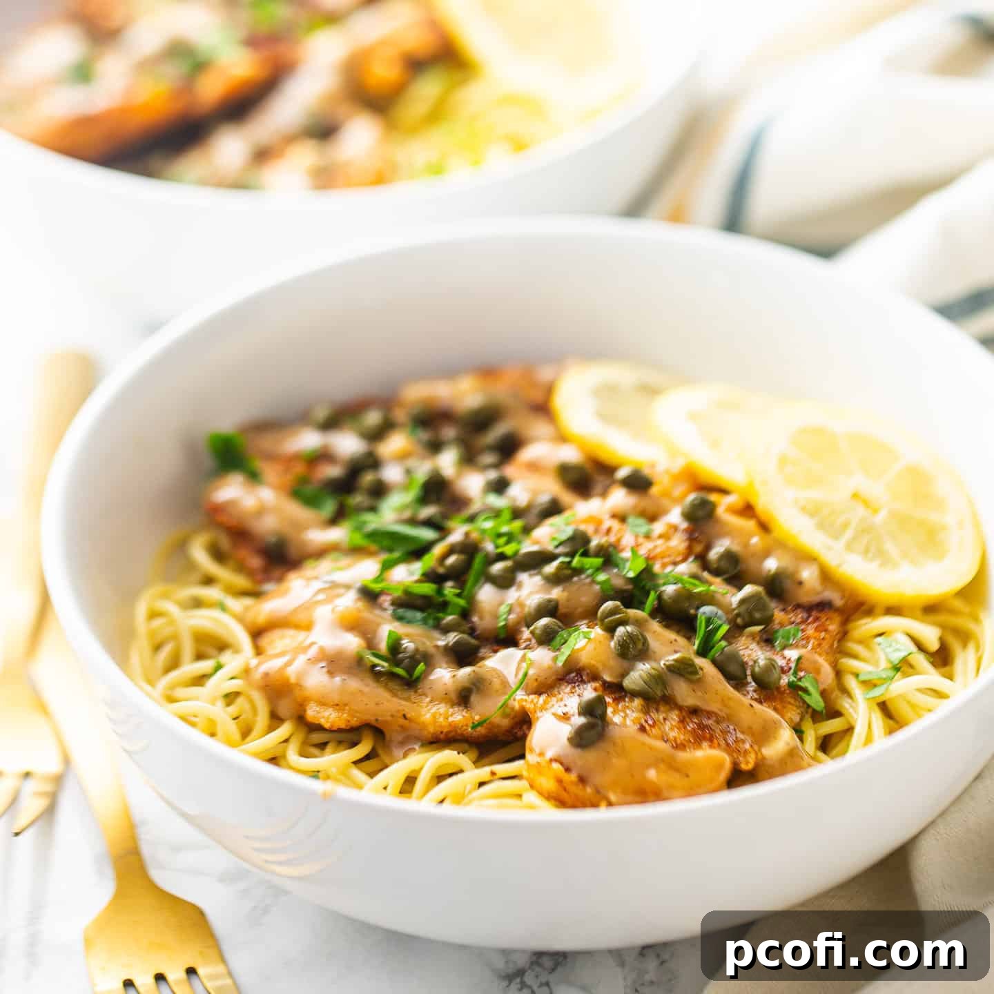 Classic chicken piccata served over pasta in a white bowl, highlighting the savory lemon caper sauce and golden-brown chicken.