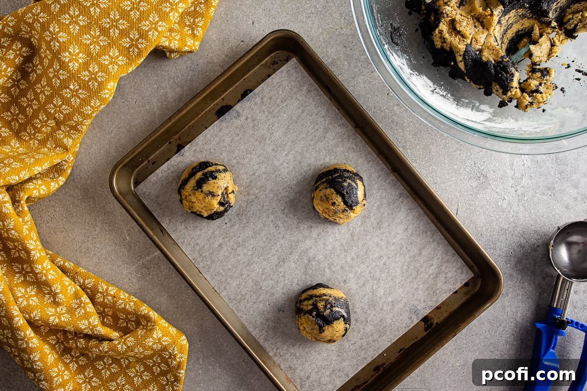 Portioned Earl Grey cookie dough with black sesame swirls on a parchment-lined baking sheet, ready for baking.