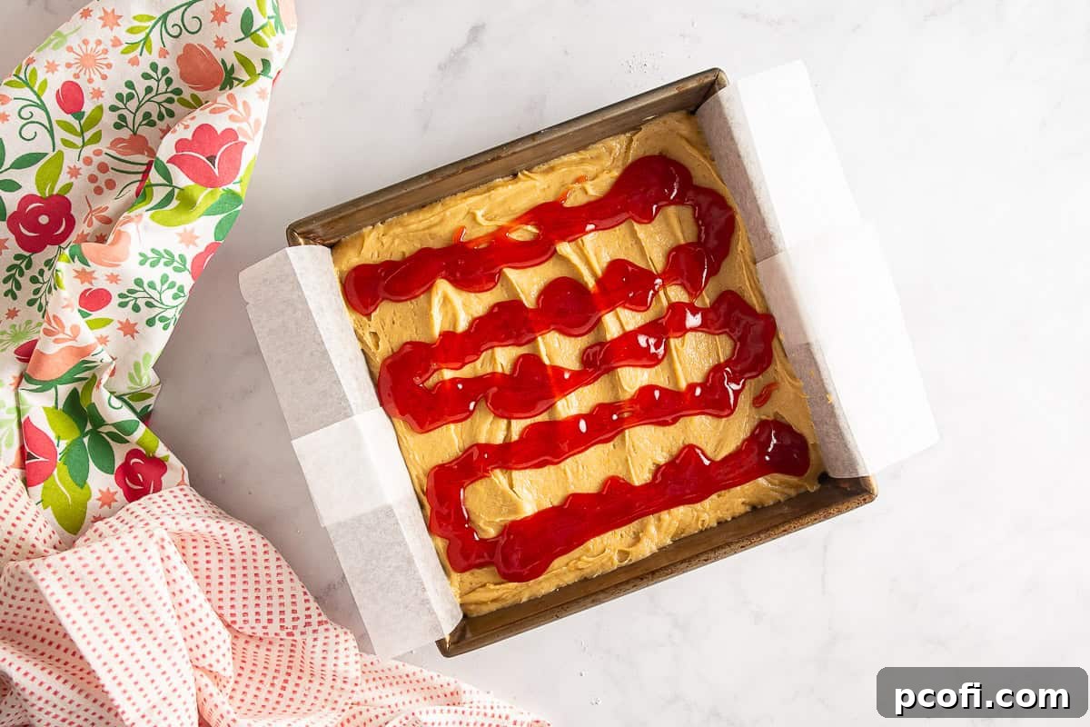 Strawberry jam carefully drizzled over the blondie batter, ready for swirling.