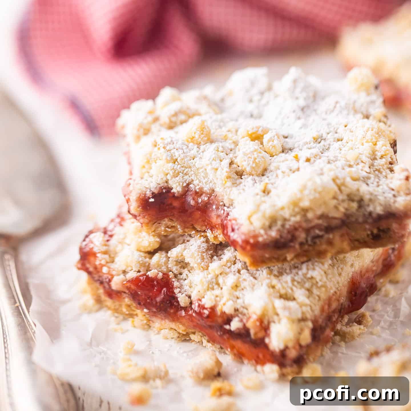 Strawberry bars in a stack with a red checked cloth, showing off their layers and inviting texture.