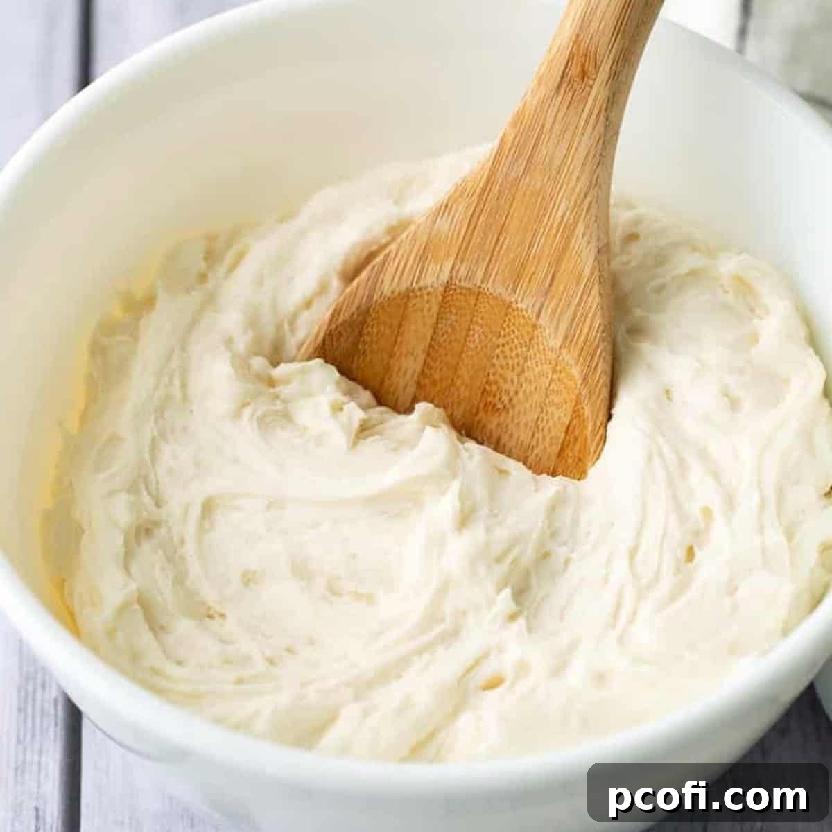 vanilla buttercream frosting in a bowl with a wooden spoon.
