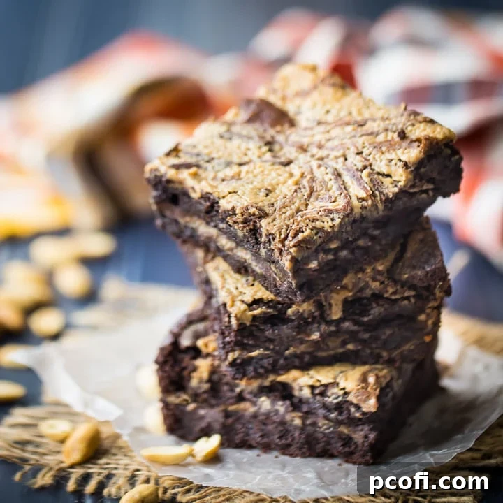 Stack of peanut butter brownies stuffed and swirled with peanut butter, on a blue background with an orange napkin in the background.