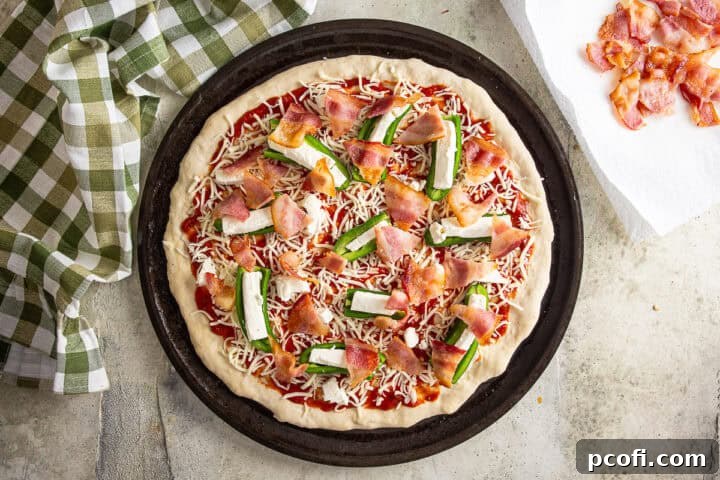 Layering par-cooked bacon onto the top of the pizza before being baked.
