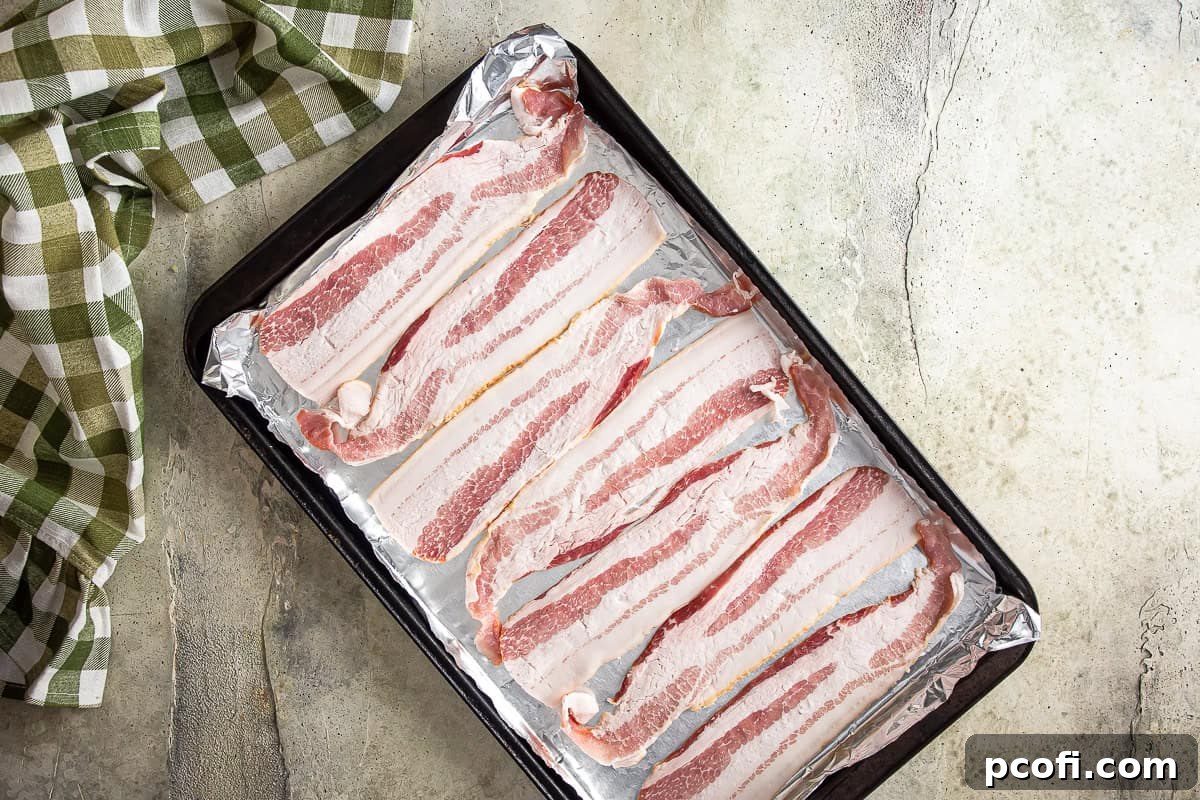 Bacon on a lined baking sheet before being partially cooked for jalapeno popper pizza.