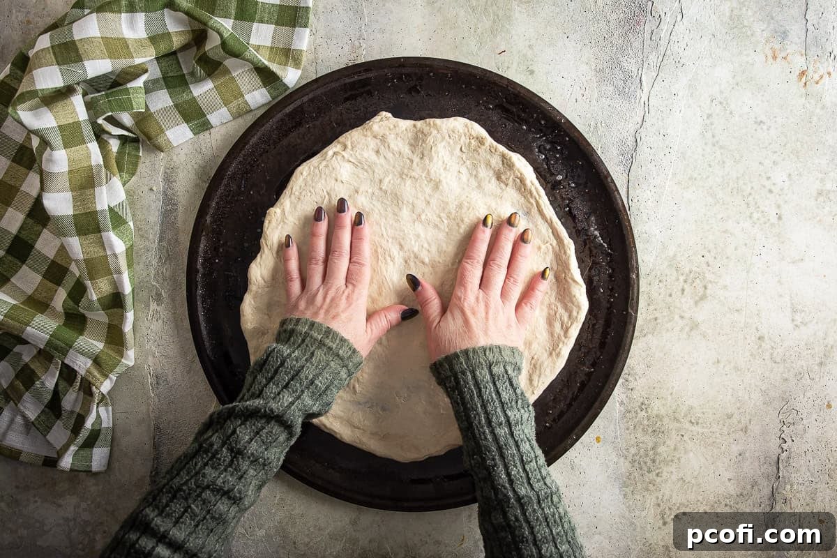 Pizza dough being stretched by hand into a thin round.