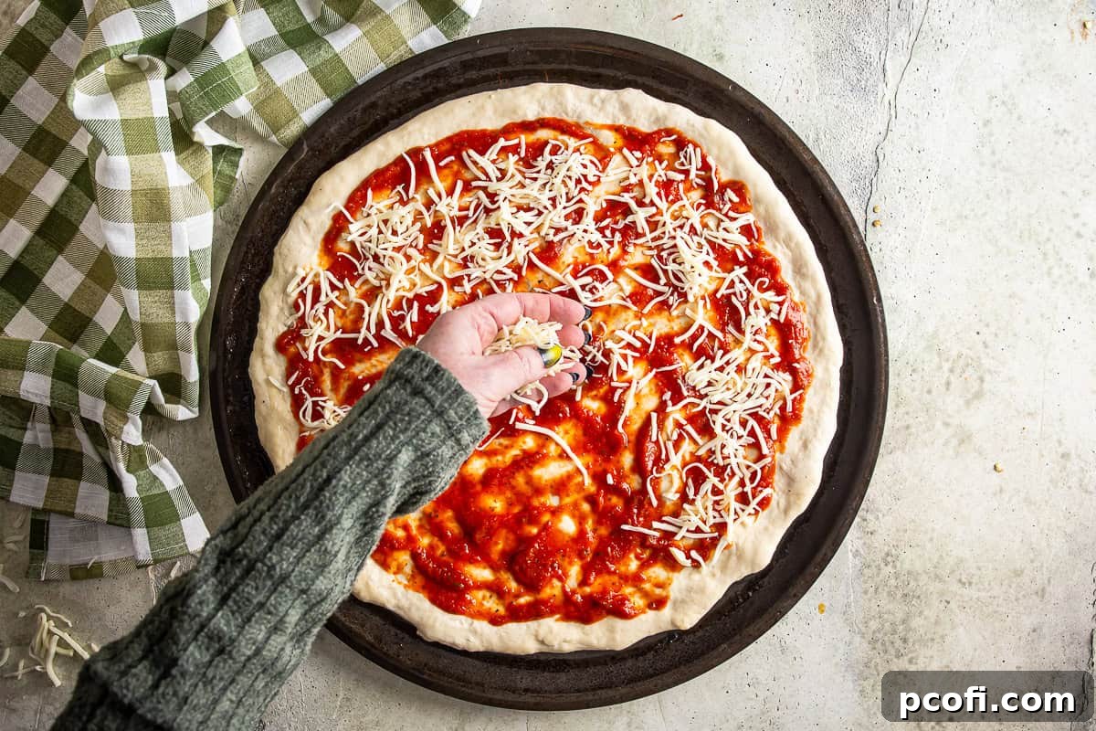 Shredded mozzarella being spread over pizza sauce on raw pizza dough.