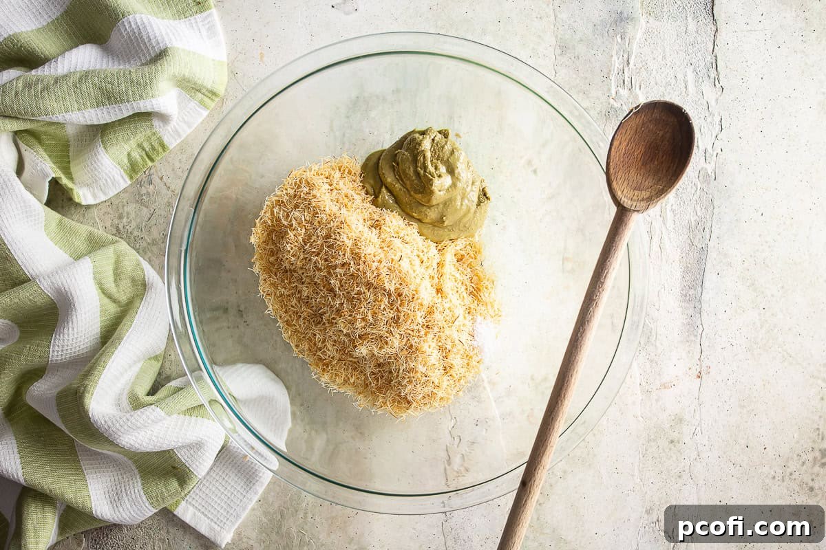 All the filling ingredients, including toasted kataifi, pistachio cream, sesame oil, and salt, being mixed together in a bowl for Dubai chocolate.