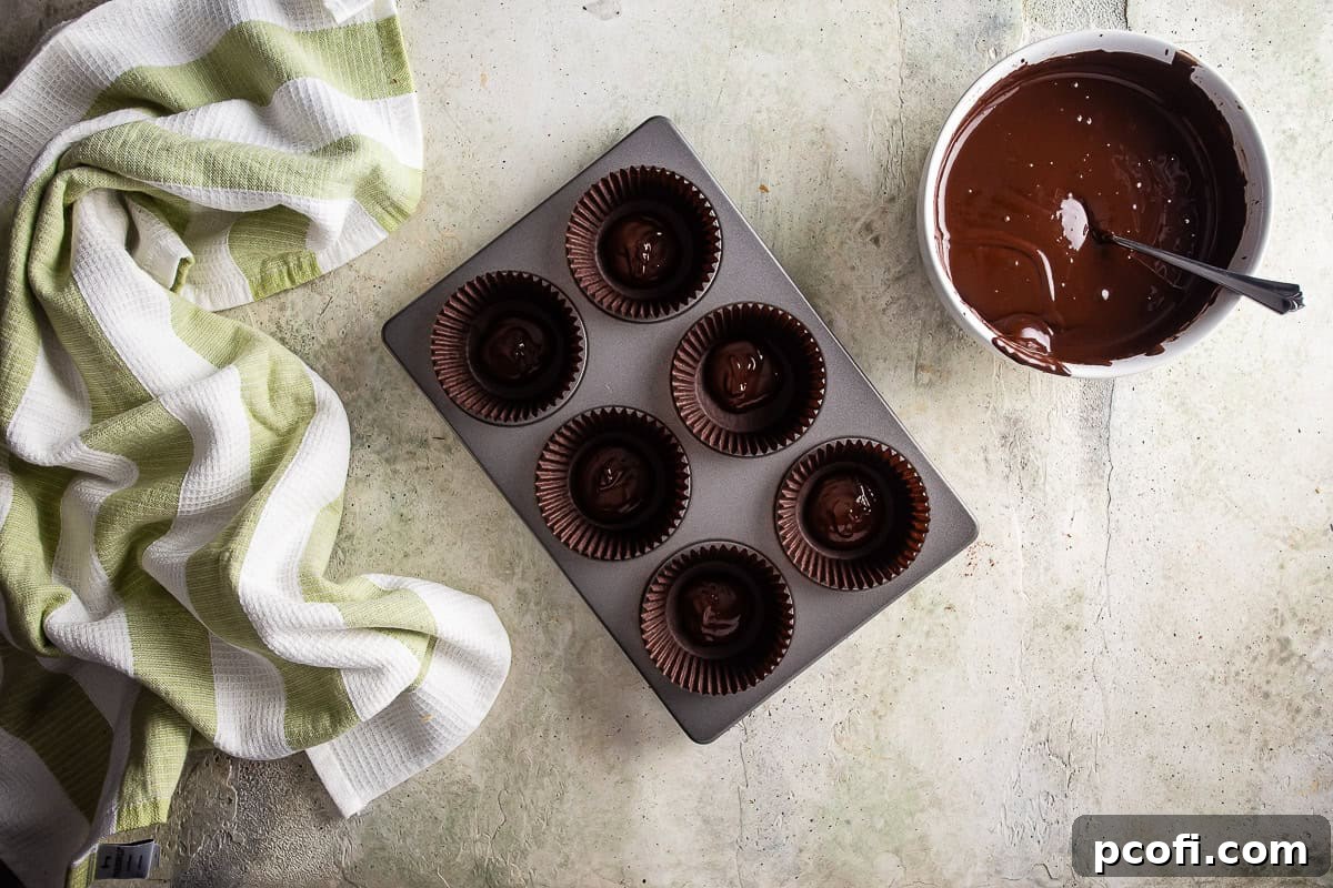 Melted chocolate being spooned into the bottom of grease-proof cupcake liners, forming the base for Dubai chocolate.