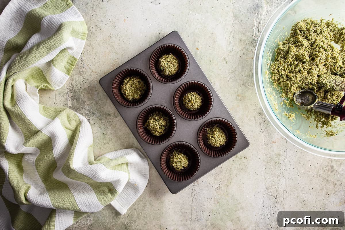 Adding the creamy pistachio-kataifi filling on top of the chocolate base in cupcake liners for Dubai chocolate.
